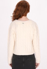 Maglione di cotone lavorato a trecce color crema con maniche lunghe, scollatura rotonda e polsini a costine. Tessuto morbido, taglio cropped e dettaglio del logo discreto sulla schiena.