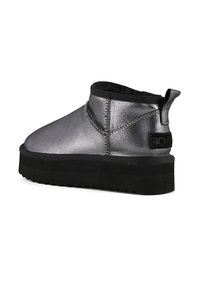 Botines metálicos plateados con suela de plataforma de goma negra y acabado texturizado. Presenta una lengüeta y detalles de costura.
