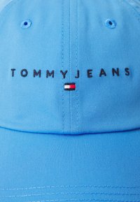Blue cotton baseball cap featuring "TOMMYJEANS" embroidered in black, with a small red, white, and blue accent on the front.