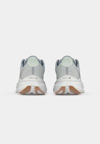 Une paire de chaussures de course gris clair vue de l'arrière, avec des semelles intermédiaires blanches et des accents de semelles extérieures bruns et blancs.