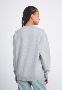 Lys grå sweatshirt med rund halsudskæring, nedsatte skuldre og ribbede manchetter. Blødt stof med en afslappet pasform, båret med stribede bukser.