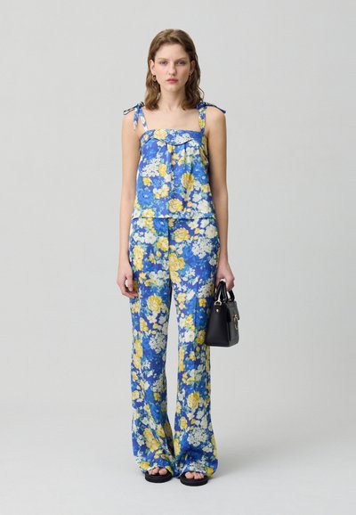 Salopette floreale blu con fiori gialli e bianchi, dotata di spalline sottili, scollatura arricciata e pantaloni a gamba larga.