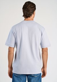 T-shirt grigio chiaro a maniche corte con una vestibilità comoda. Tessuto di cotone morbido, scollo a girocollo e cuciture visibili lungo le maniche e l'orlo.