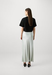 Svart croppet t-skjorte med korte ermer, kombinert med et flytende lysgrønt satin maxi-skjørt og kraftige svarte hælsandaler.