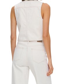 Weißes, ärmelloses Oberteil aus Denim mit cropped Schnitt, das Rückennähte und subtile Textur zeigt; kombiniert mit hochtaillierten weißen Jeans mit Gesäßtaschen.