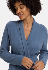 Accappatoio di tessuto morbido, di colore azzurro chiaro, con maniche lunghe, colletto a scialle e cintura, caratterizzato da un motivo a maglia testurizzata e un fit leggermente largo.