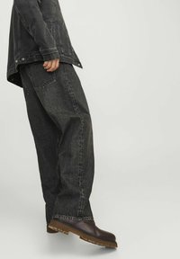 Jachetă din denim negru și blugi lejeri, asortați cu încălțăminte maro închis, având o talpă texturată și un finisaj neted.