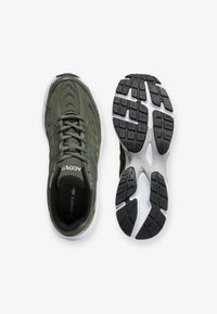 Sneaker in tessuto verde con design a lacci, caratterizzate da una suola intermedia bianca e una suola esterna nera texturizzata. Logo ben visibile sulla linguetta.