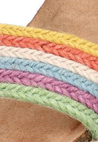Chancla de tiras trenzadas multicolores en naranja, rosa, azul, verde y amarillo, con una base de pie en un tono natural tostado.