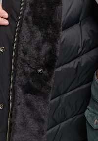 Musta puhallus takki, jossa on pehmeä, pörröinen vuori kauluksessa. Ulkopinta on sileä ja siinä on metallivetoketjuja sekä neppareita.