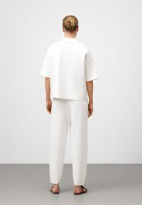 Weißes Kurzarmoberteil und passende lockere Hose aus weichem Stoff. Minimalistisches Design mit entspannter Silhouette und ohne sichtbare Muster.