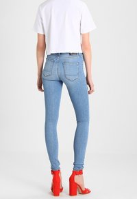 Ljusblå smala jeans med hög midja, bakfickor och kontrasterande sömmar, parat med röda klacksandaler och en vit kortärmad t-shirt.