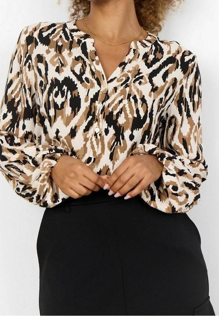Blouse à manches longues en imprimé animal beige et marron, avec une patte de boutonnage et des poignets froncés. Associée à une jupe noire.