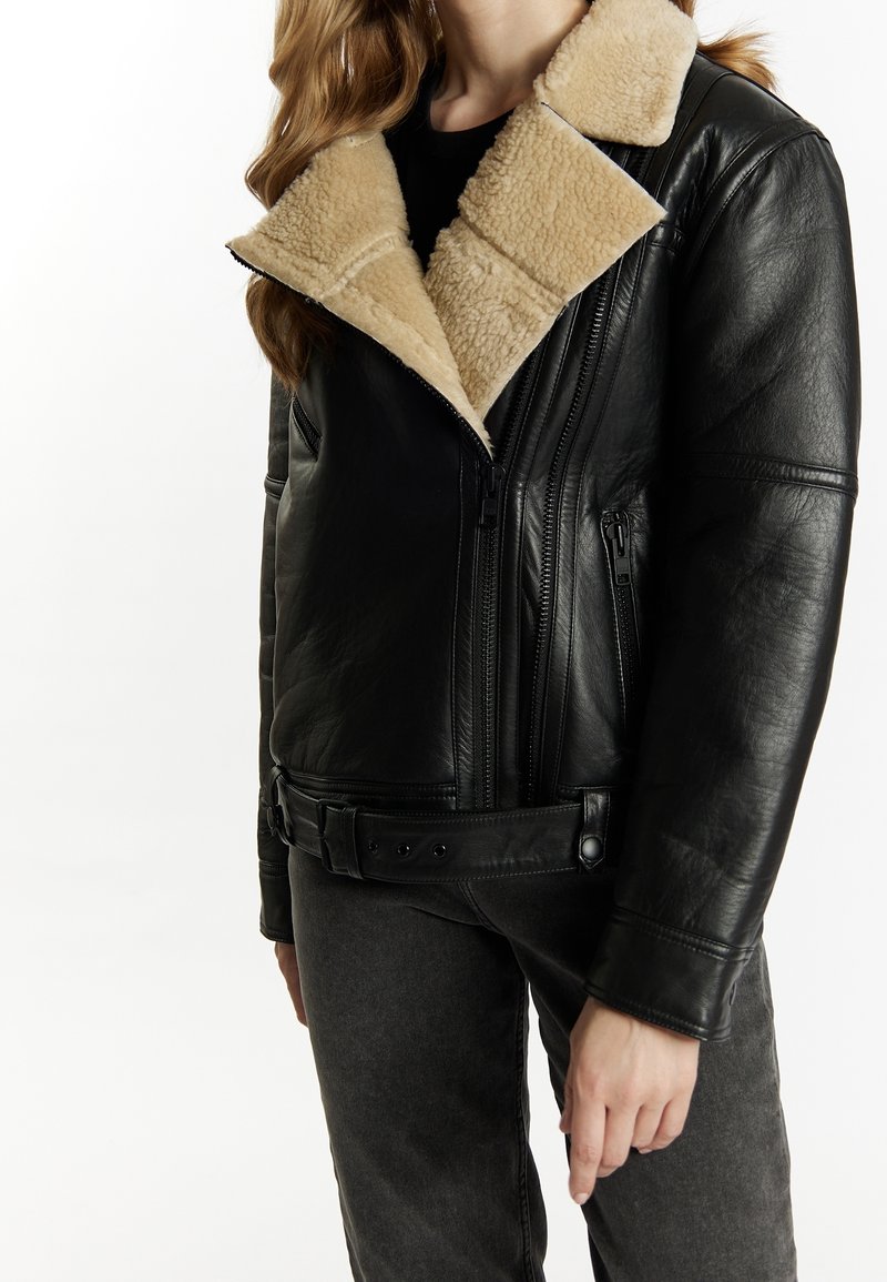 Giacca di pelle nera con collo in shearling beige, tasche con zip e vita con cintura. Texture liscia con un design aderente.
