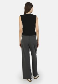 Top sin mangas negro combinado con pantalones de pierna ancha gris. Diseño simple con una textura suave. Los zapatos tienen una base beige y un acento negro.