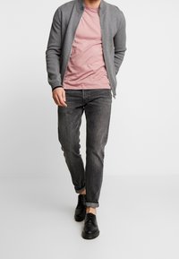 Grå zip-up bomberjacka över en rosa t-shirt, ihop med mörkgrå denimjeans och svarta snörskor. Slät tyg med ribbade detaljer.