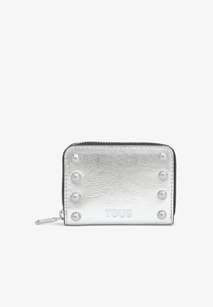 Cartera compacta plateada con cremallera, seis tachuelas redondas y el logo "TOUS" en relieve en la parte delantera, con textura de cuero visible.