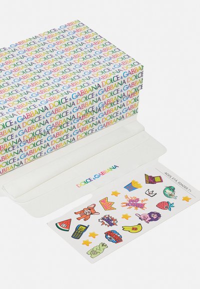 Boîte colorée avec le texte "Dolce & Gabbana" dans diverses couleurs ; inclut une feuille d'autocollants blancs avec des designs et des personnages ludiques.