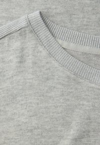 Nahaufnahme eines hellgrauen Strickpullover-Ausschnitts mit geripptem Kragen und Schulternaht-Detail.