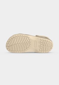 Σόλα από μπεζ παπούτσι Crocs με υφή για καλύτερο κράτημα, ενδείξεις μεγεθών 9 και 10 και το λογότυπο Crocs ορατό στο κέντρο.