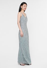 Abito da sera lungo in azzurro chiaro con intricate perline argento, scollatura a V e spalline sottili; silhouette aderente con gonna fluente.