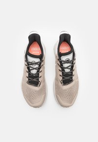 Beige Sportchuhe mit Netzobermaterial, abgerundeter Spitze, schwarzen Akzenten und strukturierten Sohlen. Mit gemusterten Schnürsenkeln und gepolstertem Zungenbereich.