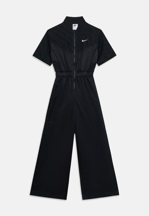 Combinaison noire Nike à manches courtes, fermeture éclair frontale, taille élastique, jambes larges et logo Nike swoosh blanc sur la poitrine.