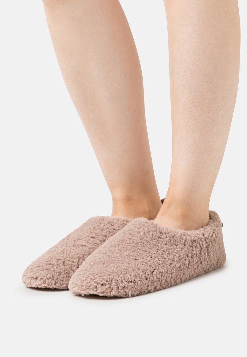 Fuzzy, light brown slippers with a low cut design, soft texture, and pointed toe shape. Positioned on bare feet with a smooth finish.