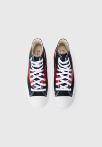 Fekete vászon tornacipő piros díszítéssel, fehér fűzőkkel és gumitalppal. Kontrasztos varrással és keskenyített orr-résszel rendelkezik.