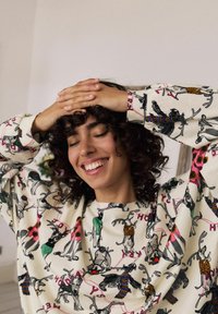 Sudadera de color crema que presenta animales de dibujos animados como renos y perros, adornados con suéteres y detalles coloridos, con un corte relajado y mangas largas.