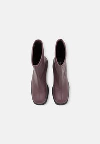 Botines burdeos de cuero liso con un diseño elegante, punta redondeada y suela de goma negra. Presentan un detalle de costura vertical.