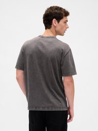 Pilko medvilnės marškinėliai su laisvu siluetu, apvalia iškirpte, trumpomis rankovėmis ir subtilia tekstūra. Gale matomi sustiprinti siuvimo siūliai.