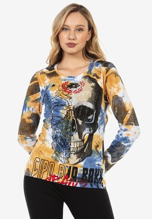 Langsleeve top met een kleurrijke schedelafbeelding, blauwe en oranje abstracte patronen en tekst onderaan. Gemaakt van zachte, rekbare stof.