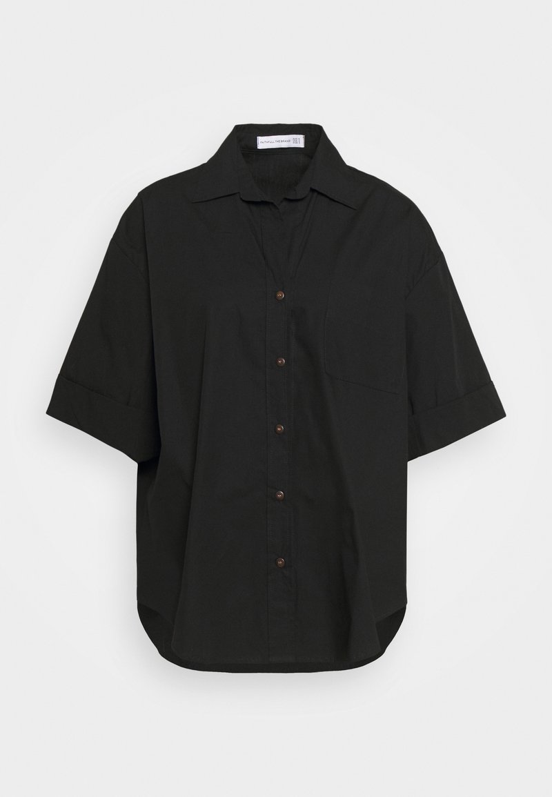 Chemise noire oversize à manches courtes boutonnée avec poche poitrine et col ouvert sur fond clair uni.