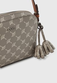 Borsa a tracolla grigia in pelle con motivo a foglia bianca, chiusura con zip, piccoli dettagli a frangia e una tracolla regolabile marrone. Logo del marchio visibile.