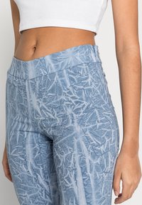 Leggings azuis com padrão, feitos de tecido texturizado, apresentando uma cintura alta e uma aparência enrugada com desenhos semelhantes a folhas.