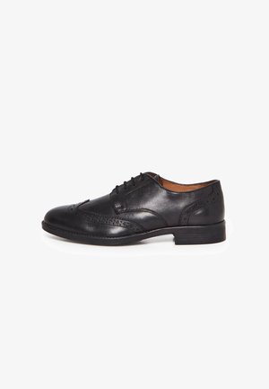 Chaussure habillée pour homme en cuir noir à bouts fleuris avec perforations brogue et lacets, vue de côté sur un fond blanc.