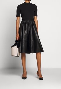 Czarny prążkowany top z krótkimi rękawami w połączeniu z wysokim, plisowanym czarnym skórzanym spódnicą. Uzupełniony małą jasną torebką i szpilkami.