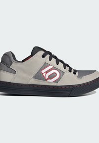 Grey and black shoes with a suede and mesh upper, featuring a red logo and stitching, and a textured rubber sole.