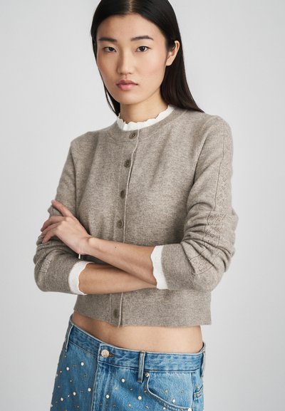Lichtbruin cropped vest met gestructureerde stof, ronde halslijn, knoopsluiting en witte ruffles aan de manchetten.