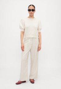 Pull en maille beige clair avec des manches bouffantes, associé à un pantalon large beige clair. Chaussures bordeaux avec une finition brillante et un détail de boucle.