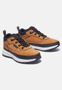 Brązowe zamszowe sneakersy z czarnymi akcentami, gumową podeszwą, wyściełanym kołnierzem oraz białą kontrastową podeszwa środkową, z czarnymi sznurówkami i detalem logo.