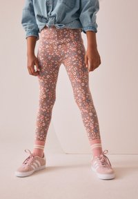 Blomstrede leggings i pink, blå og beige med en tætsiddende pasform. Kombineret med lyserøde sneakers og stribede sokker. Denimtop knyttet i taljen.