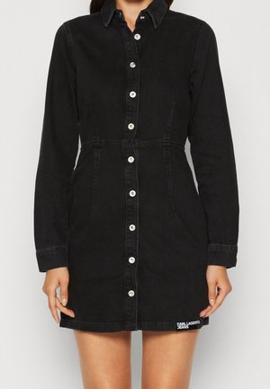 Abito da camicia in denim nero con maniche lunghe, chiusura frontale con bottoni, colletto a punta e tasche laterali. Presenta un dettaglio del logo bianco all'orlo.