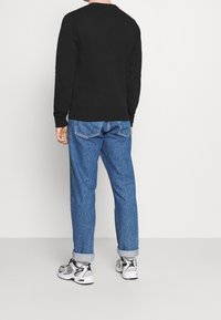 Sudadera negra con cuello redondo, puños y dobladillo de canalé, combinada con jeans de mezclilla azul, remangados en los puños, y zapatillas deportivas blancas.