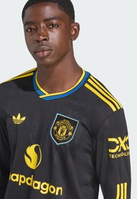Black Manchester United jersey with yellow accents and blue trim. Features Adidas logo and sponsor logos. Short sleeves and embroidered badge.