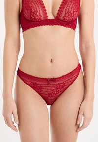 Completo lingerie in pizzo rosso composto da un reggiseno a triangolo e un perizoma abbinato. Motivi floreali delicati e bordi smerlati. Tessuto morbido.