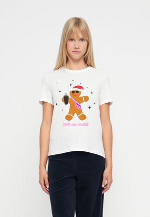 Kvinne iført en hvit T-skjorte med et pepperkakemannsdesign som holder en drink, iført solbriller og nissehatt, med teksten "Ser ut som en snacks."