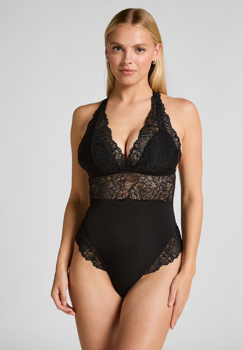 Svart spetsteddy med djup V-ringning, halterband och intrikata spetsdetaljer vid bål och benöppningar.