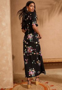 Musternäoline musta maksikleit lühikeste volangvarrukatega, millel on erksad mitmevärvilised lilled. Kanda rihmadega platvormsandaalidega.